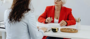 Teilpension 2026 | Ältere Frau bespricht etwas mit jüngerer Frau an Bürotisch