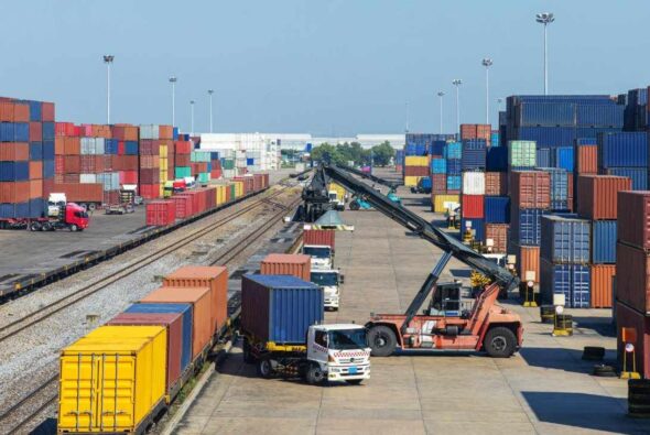 Containerhandling durch Fahrzeuge am Bahnterminal inmitten von gestapelten Containern.