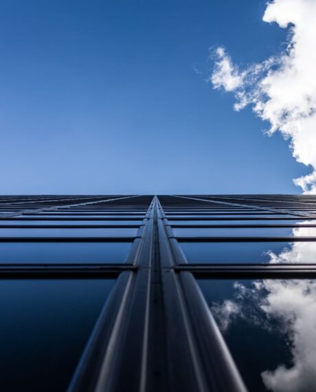 Blick entlang einer Glasfront eines Gebäudes in den blauen Himmel mit Wolken